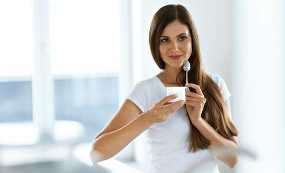 Woman enjoying a spoonful of yogurt, representing a light, healthy snack as part of a balanced, fibre-supporting diet