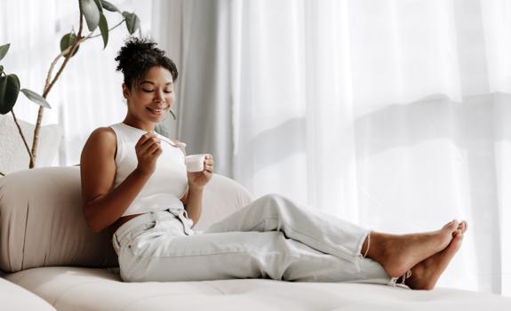 Woman relaxing on a sofa while eating yogurt, illustrating a healthy snack choice that can support daily fibre intake